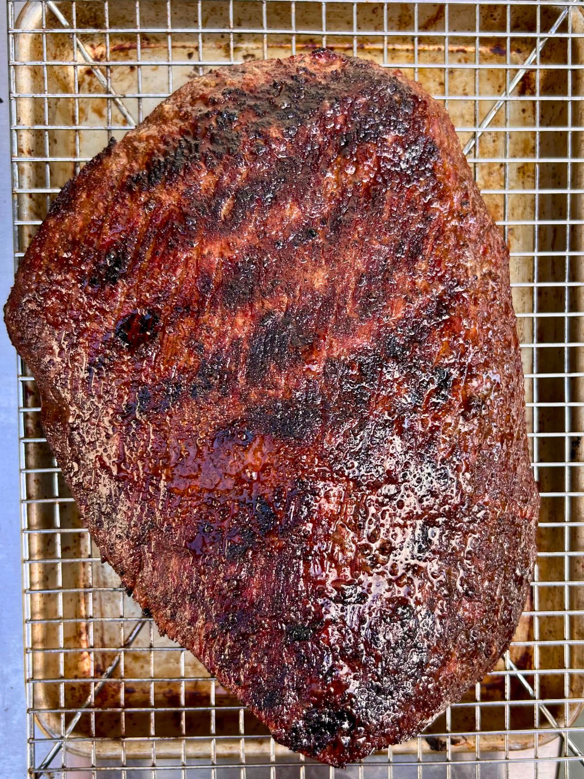 Grilled espresso rubbed flank steak is resting on a wire rack placed over a rimmed baking sheet.