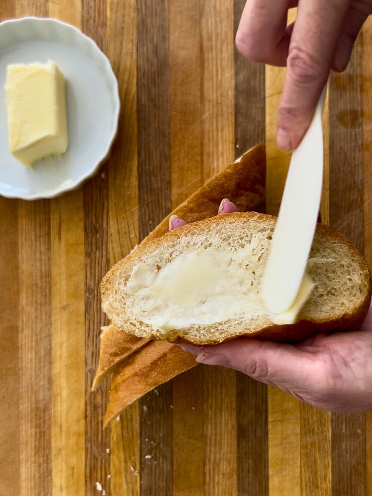 A spatula is used to butter oval slices of bread for open-faced steak sandwiches.
