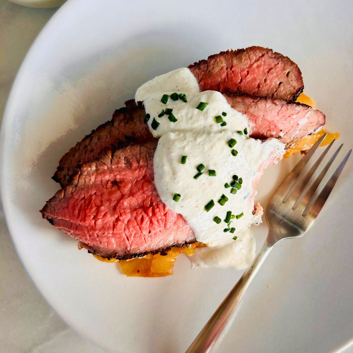 A partially eaten open-faced steak sandwich and a fork on a white plate.