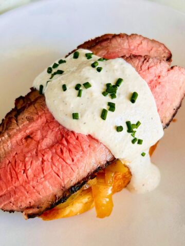 Open-faced steak sandwich with espresso rubbed flank steak, caramelized onions, and creamy horseradish garnished with chives.