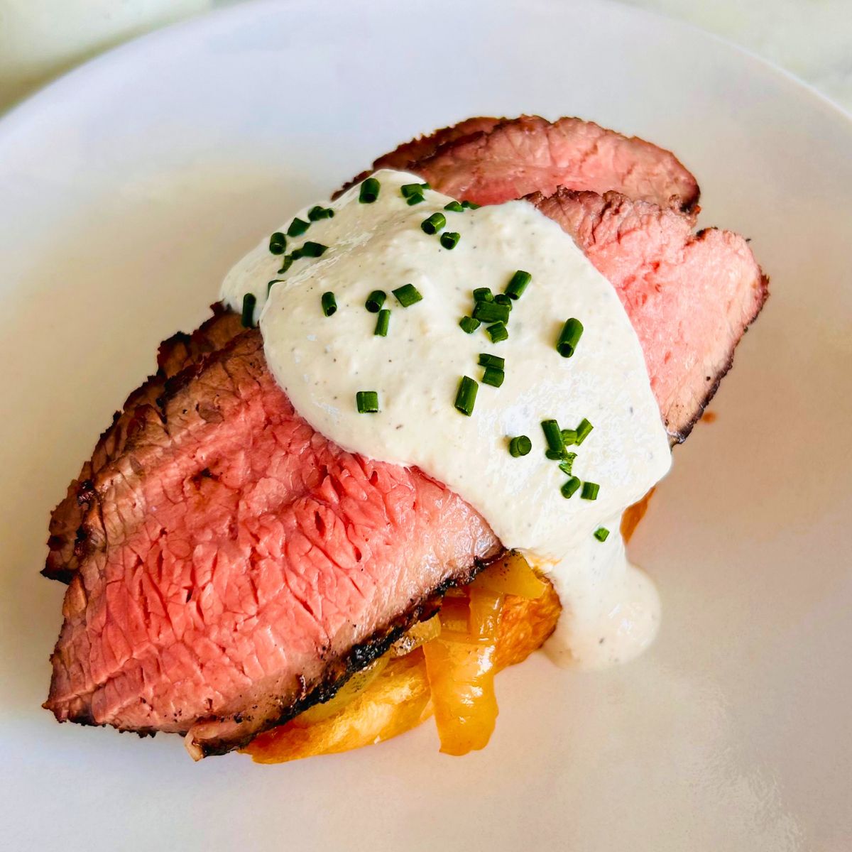 Open-faced steak sandwich with espresso rubbed flank steak, caramelized onions, and creamy horseradish garnished with chives.