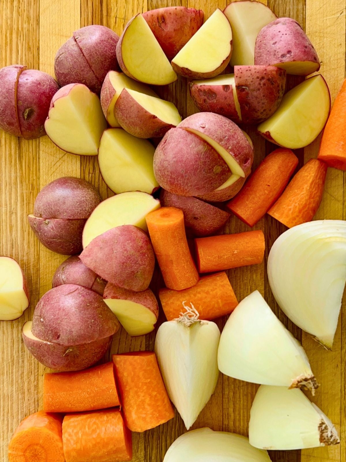 Potatoes, carrots, and an onion are chopped into chunks on a cutting board.