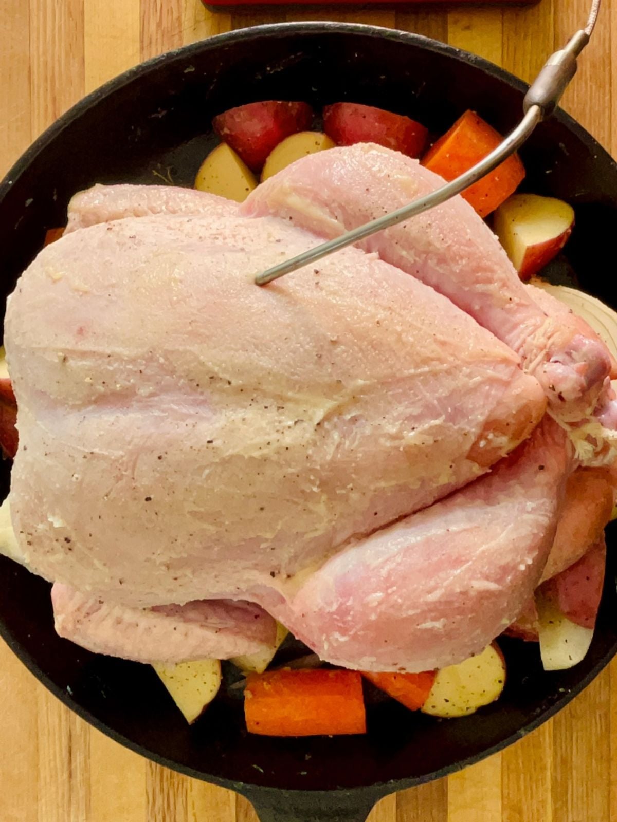 Ghee is rubbed on a whole chicken with a thermometer inserted ready to cook in a skillet.