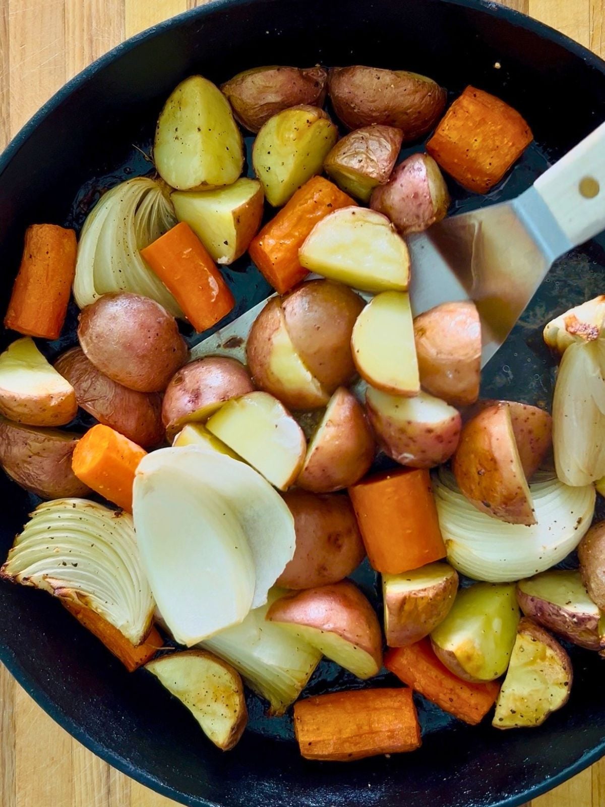 A spatula is flipping vegetables to coat them with chicken drippings in a cast iron skillet.