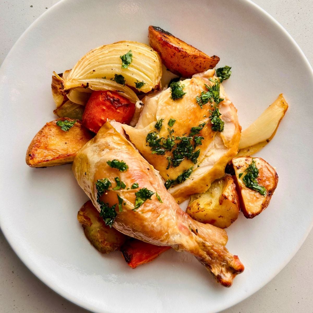 Pieces of juicy skillet roasted chicken with caramelized vegetables on a white plate.