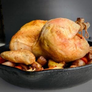 A cast iron skillet holding a whole roasted chicken with caramelized vegetables.