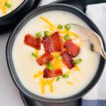 A spoon is going into a bowl of copycat Panera baked potato soup with bacon, cheese, and green onions.