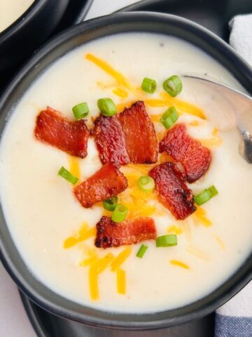 A spoon is going into a bowl of copycat Panera baked potato soup with bacon, cheese, and green onions.