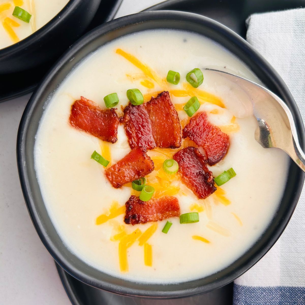 A spoon is going into a bowl of copycat Panera baked potato soup with bacon, cheese, and green onions.