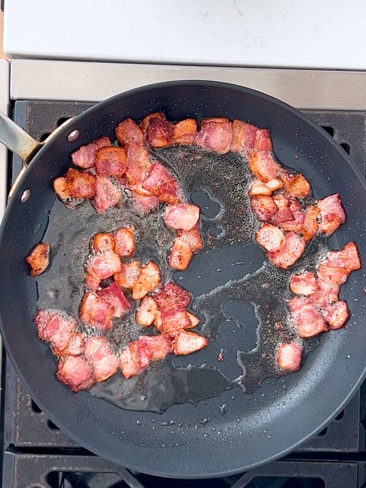 Pieces of bacon cooking in a skillet.