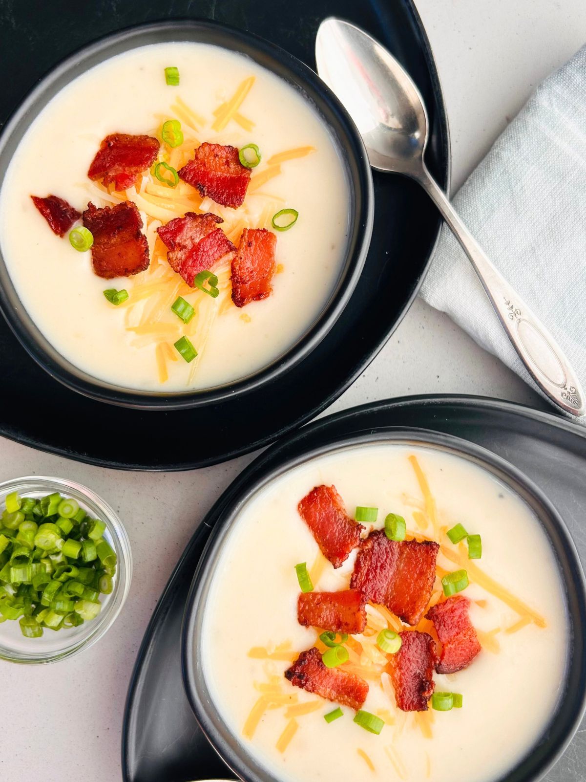 Two black bowls of copycat Panera soup topped with bacon, cheese, and green onions.